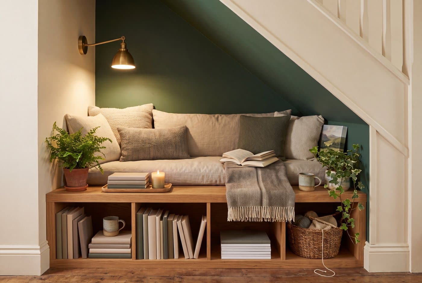 An understairs reading nook with a built-in bench along the back wall, book cubbies underneath and a wall light under the slope